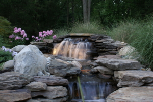 Landscape lighting lights up the waterfall in this landscaped backyard