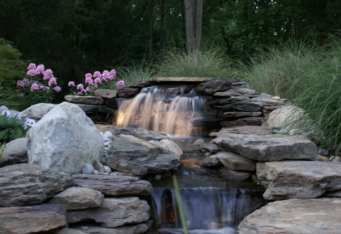 Landscape lighting lights up the waterfall in this landscaped backyard