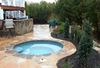 A hot tub surrounded by plantings for privacy in this backyard design