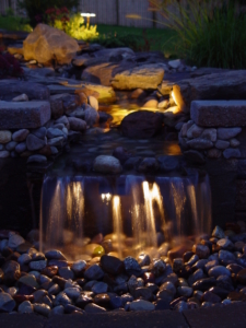 Landscape Lighting lights up a waterfall completing the landscaping of this home